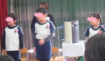 遊戯室で椅子の前に立って歌を歌うこども3名