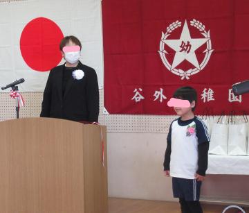 遊戯室のステージに立って発表する子どもと隣で見守る園長先生