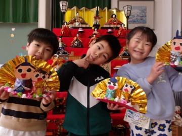 年長児が雛飾りの前で写真を撮る姿