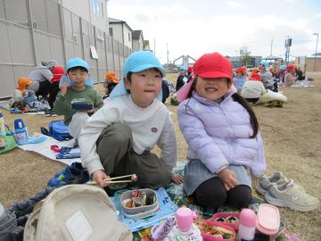 屋外で、一緒にお弁当を食べている園児たちの様子