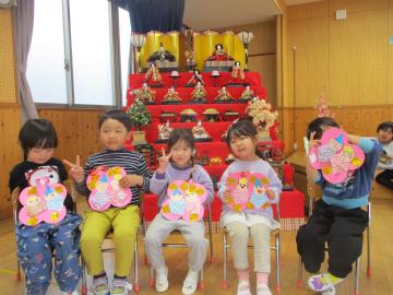 遊戯室で、お雛様と写真を撮っている園児たちの様子