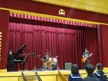 体育館のステージで梶原さんと職員がコラボ演奏をしています