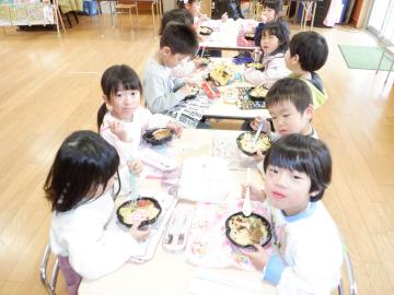 教室でテーブルに座ってみんなで雛ちらしを食べる幼児