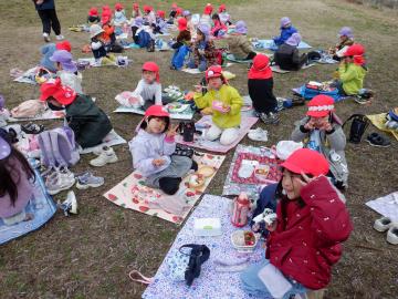 芝生の上レジャーシートを敷いてお家の方の手作り弁当を食べる子供たち