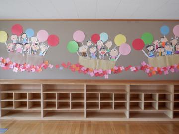 子供たちがクレパスで自分の顔や体を描き切り抜いたものを、教室の壁面に貼っているようす