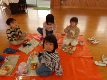 教室に敷いたレジャーシートの上で交流しながら昼食を食べる学年の違う子供たち