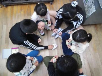 床に輪になって座りカードを出しあっている児童たちを上から撮影した様子