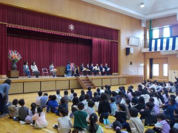 代表児童が離任される先生に花束を渡している様子を全校生が見ている。