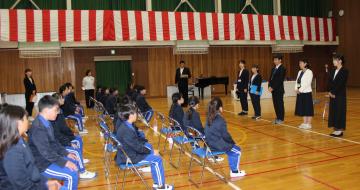 体育館で着任した先生の挨拶を聞く子どもたち