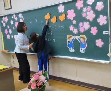 教室の黒板の前で担任と談笑する新入生