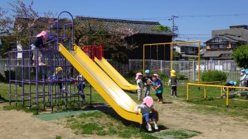 滑り台やジャングルジムなどの園庭の遊具で異年齢が交わって遊ぶ様子