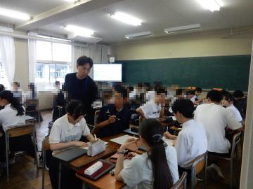 教室内で、ワークシートに取り組む別の生徒たちを指導する教員の様子