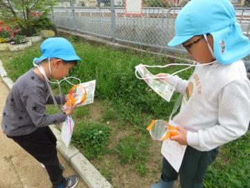草むらで虫眼鏡で昆虫を探す園児たちの様子