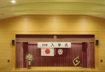 入学式の舞台上の様子。看板と国旗や校旗があります。