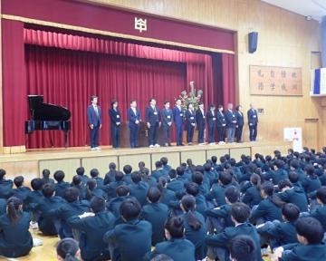 着任式の様子。体育館の壇上で14名の職員が整列しています。
