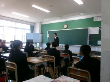 教室で黒板の前に立つ担任の先生が机に座る生徒たちに向かって熱く思いを語っている様子
