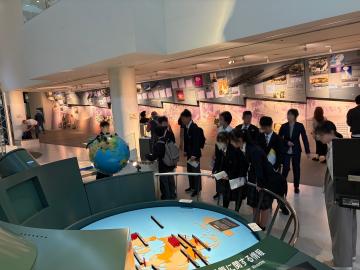 博物館の展示室で地球儀や大型のインタラクティブテーブルを囲んで複数の見学者が展示を見ている光景