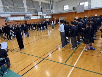 体育館で多数の生徒が制服を着て並び整列している様子