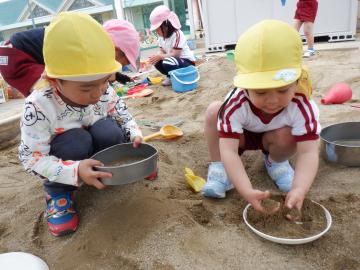 ふるいに砂を入れて振り、さら砂をつくる二人の子供