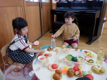 テーブルにままごとの料理を並べて遊ぶ二人の女児