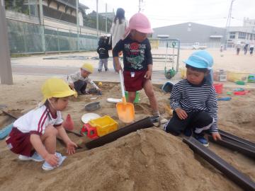 砂場でシャベルを持って山を作ったり、樋をつなげたりして遊ぶ子供たち
