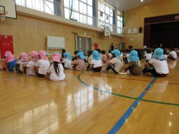 体育館でクラスごとに1列に並んで座る子供たち