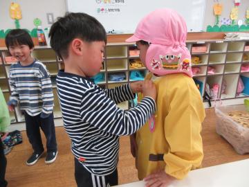 室内で年下の幼児のボタンをはずしてあげようとうする男児