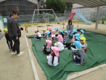砂場に座って教師の話を聞く子供たち