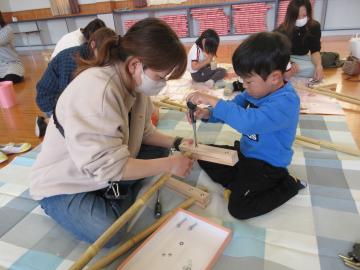 保護者が竹馬を抑えて、ドライバーでネジをとめる子ども