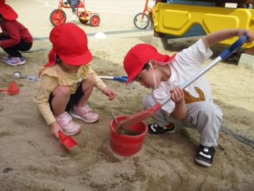 砂場で砂をバケツに移して遊んでいる園児たちの様子