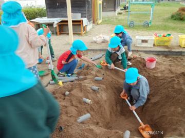 砂場で穴を掘ったり筒に水を流そうとしたりして遊んでいる園児たちの様子