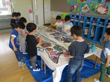 大きな紙に、墨でこいのぼりをかき、絵の具で色を塗っている園児たちの様子