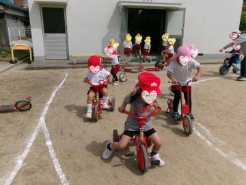 園庭で3歳児と4歳児と5歳児が三輪車で遊んでいる様子