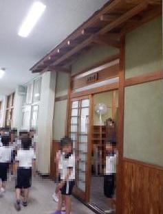 木造の引き戸がある学校の廊下で制服を着た児童たちが出入りしている様子