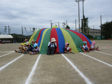 校庭で園児たちがパラバルーンをしているところ