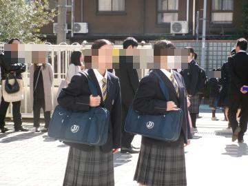 制服を着た学生たちが校門で通学バッグを持って立っている様子