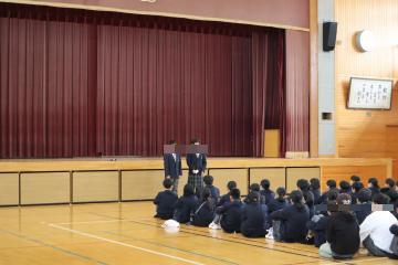 体育館の舞台前に代議委員の生徒がたち、そのほかの一年生はクラスごとに列を作り座って代議委員の生徒の発表を聞いています。