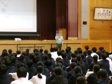体育館でスクリーンをバックに講師の先生が話をしています。