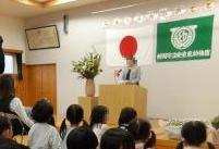 演台に立っている園長先生の話を、椅子に座って聞いている保護者と子供たちの様子