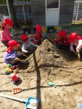 4歳児の子供たちが砂場で大きな山をつくっています