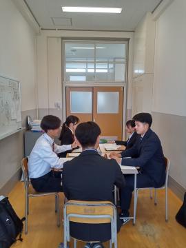 教室で机を囲んで資料を見ながら話し合う学生数人