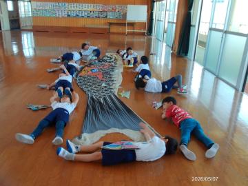 幼児が鯉のぼりの周りに寝転がり大きさを比べている