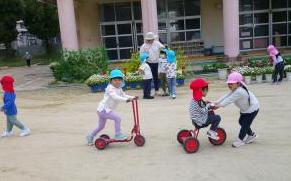 三輪車に乗っている3歳児を4歳児が引っ張っている様子
