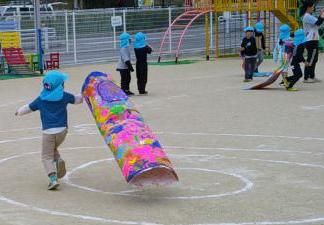 園児たちが園庭でこいのぼりを持って走って風をはらませている様子