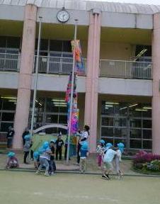 園庭で園児たちが掲揚柱にこいのぼりを揚げている様子