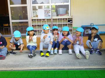 園児たちがテラスに座って笑顔でイチゴを食べている様子