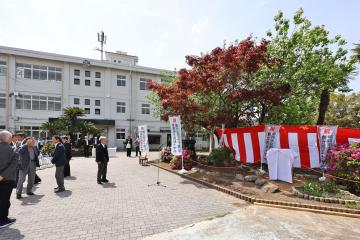 校舎前の広場で紅白の幕と看板が設置された式典会場に参列者が立っている