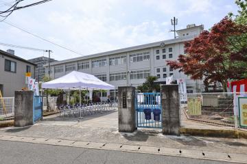 門の前にテントと椅子が並ぶ校舎の正面風景