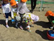 公園の砂場でオレンジの帽子をかぶった子どもたちがバケツや容器を使って水や砂で遊んでいる