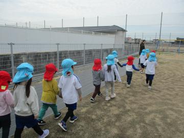 園児たちが赤と水色の帽子をかぶり手をつないで園庭を歩いている